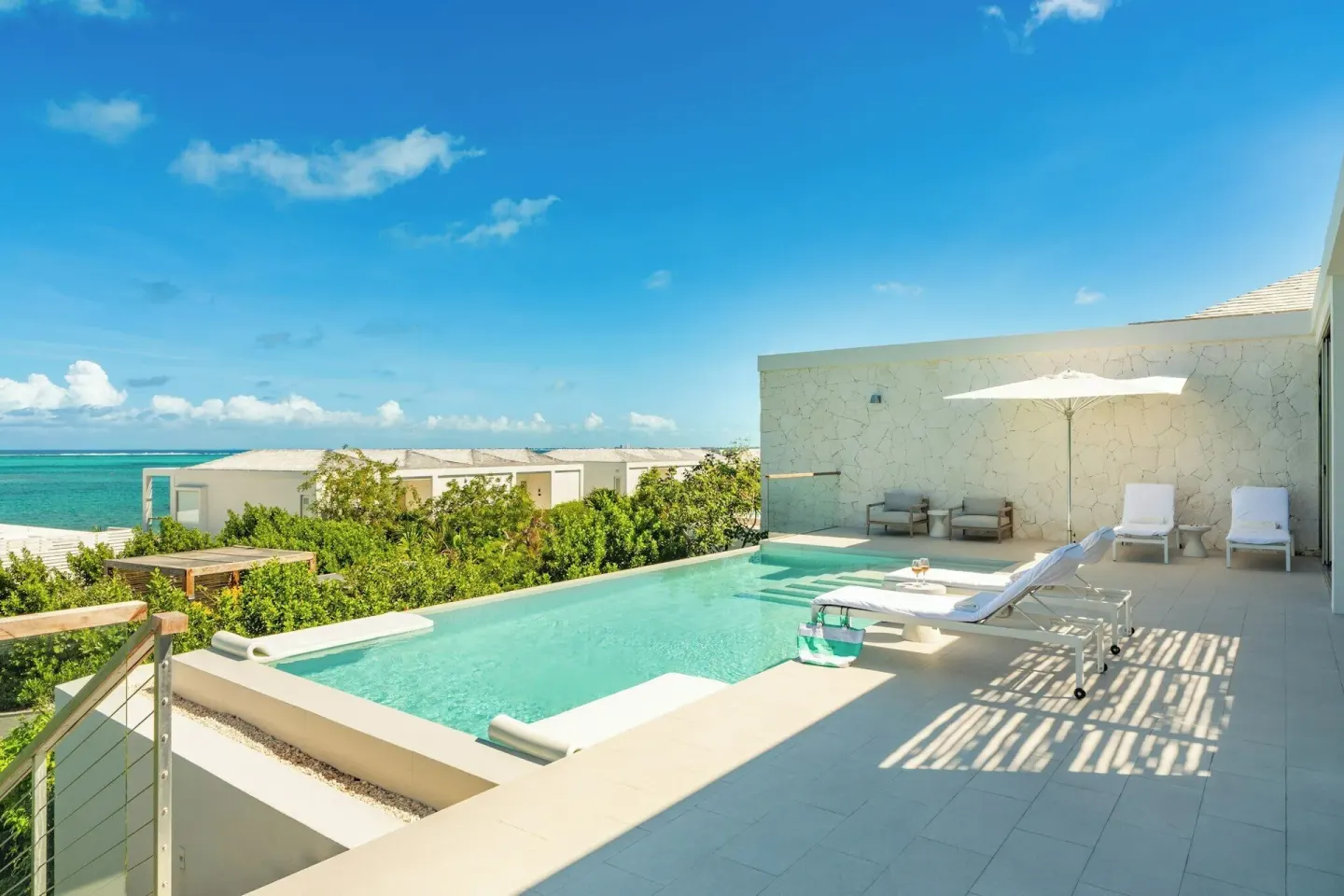 Ocean-view pool terrace with loungers, umbrella and white stone walls at Rock House.