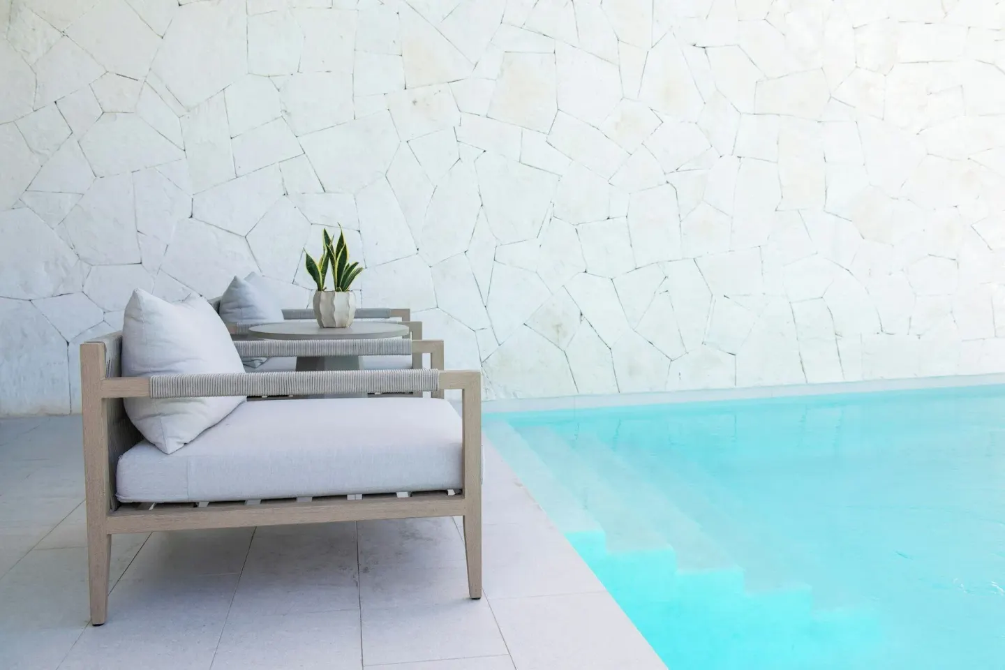 Poolside cushioned chair beside turquoise water and a white stone wall at Rock House.