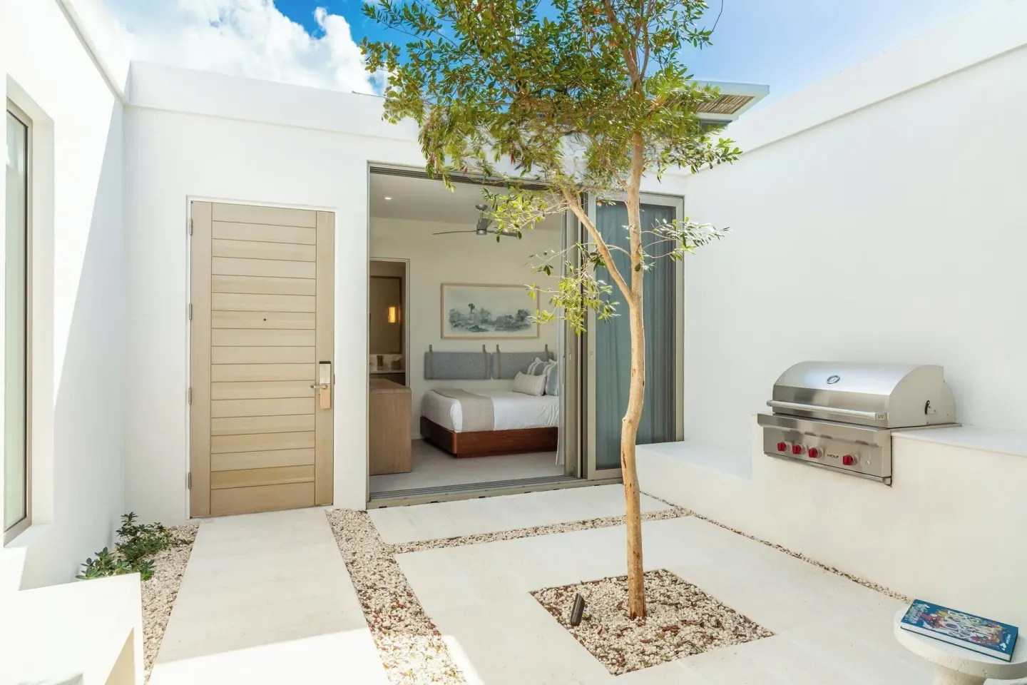 Private courtyard at Rock House with a bedroom entrance, small tree, and built-in grill.