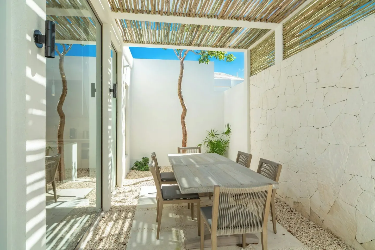 Shaded outdoor dining patio at Rock House with a table, chairs, and white stone walls.