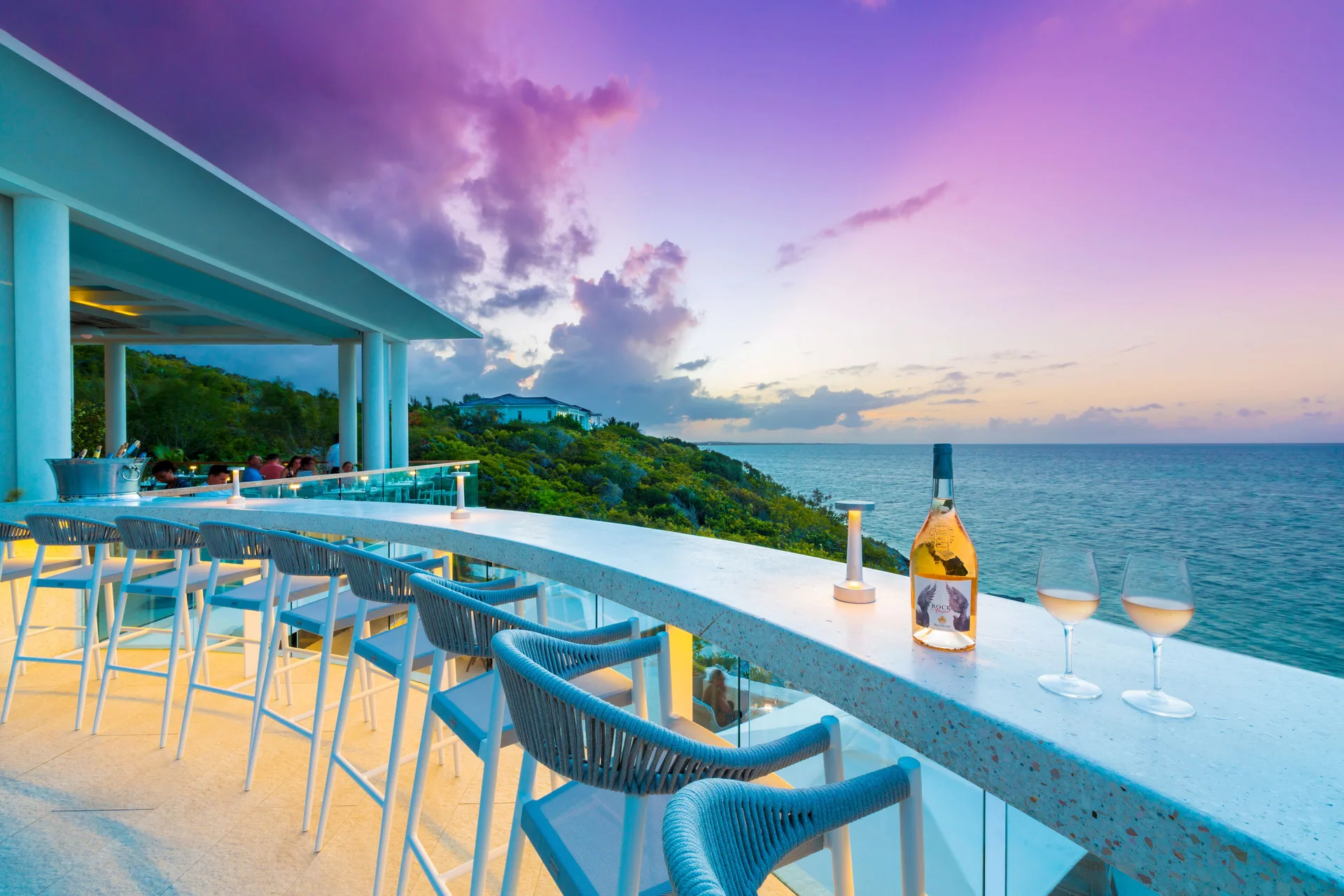 Oceanfront bar counter with stools, wine glasses, and sunset views at Rock House.