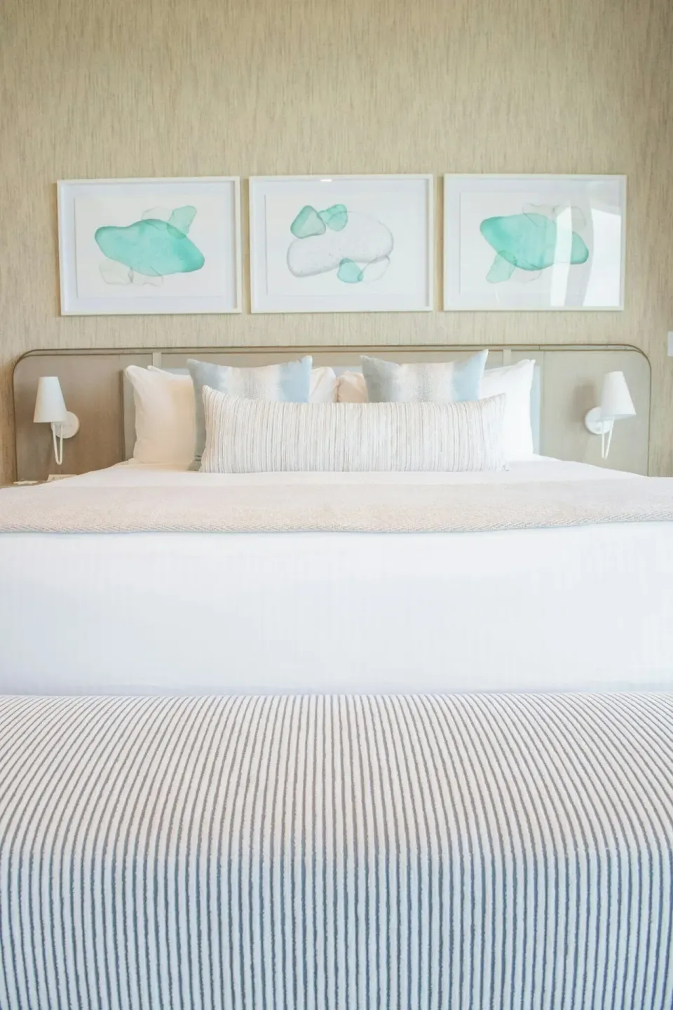 King bed with striped bench and coastal artwork in an ocean-view villa at Rock House.