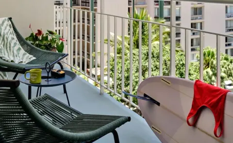 Balcony chairs, small table, and surfboard on a guest balcony at Romer House Waikiki.