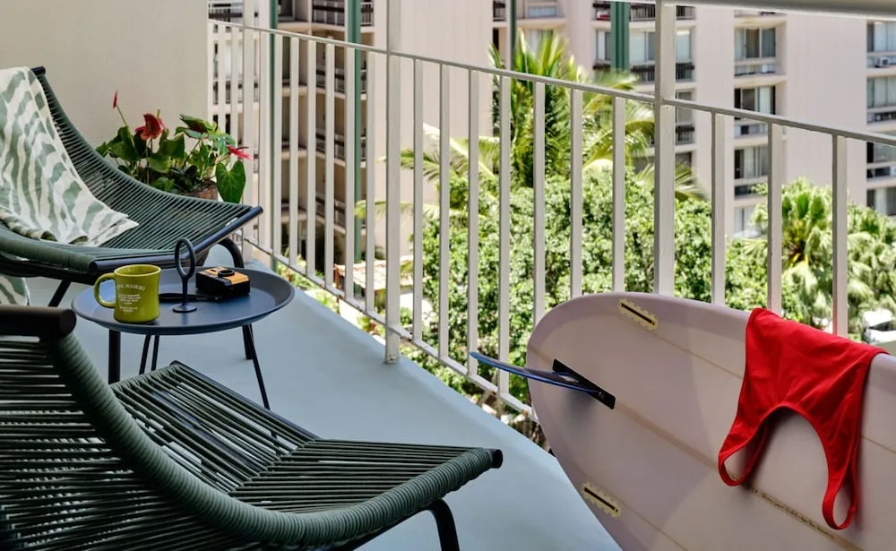 Balcony chairs, small table, and surfboard on a guest balcony at Romer House Waikiki.