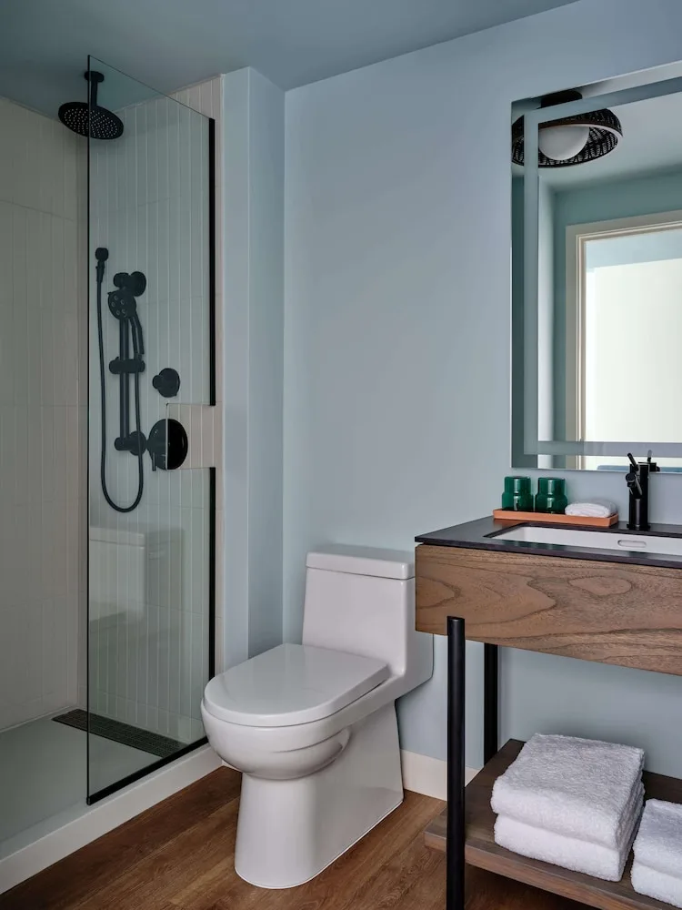 Guest bathroom with glass shower, toilet, and wood vanity at Romer House Waikiki.