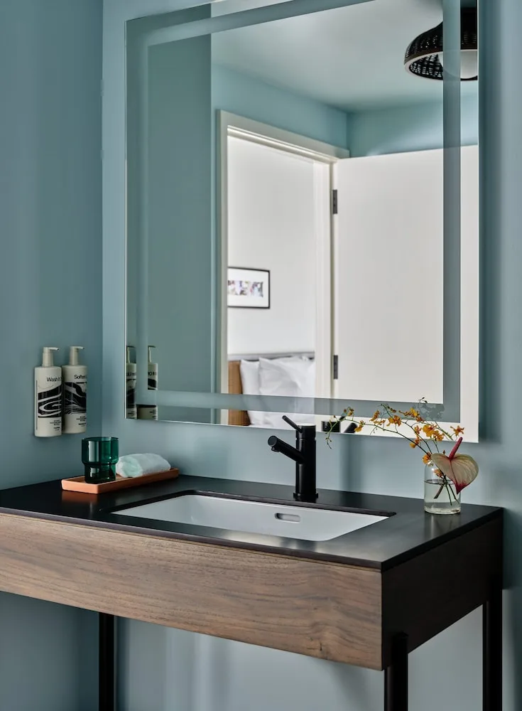Bathroom vanity with mirror, sink, and flowers in a guest room at Romer House Waikiki.