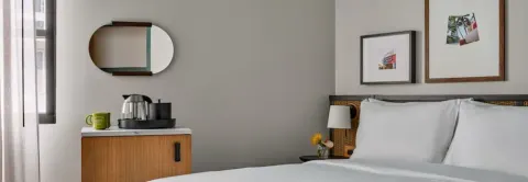 Guest room bed beside a cabinet with coffee setup and wall mirror at Romer House Waikiki.