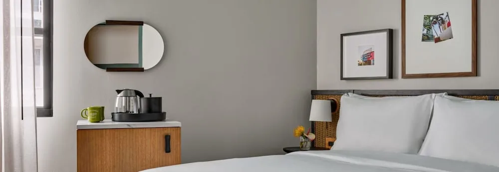 Guest room bed beside a cabinet with coffee setup and wall mirror at Romer House Waikiki.