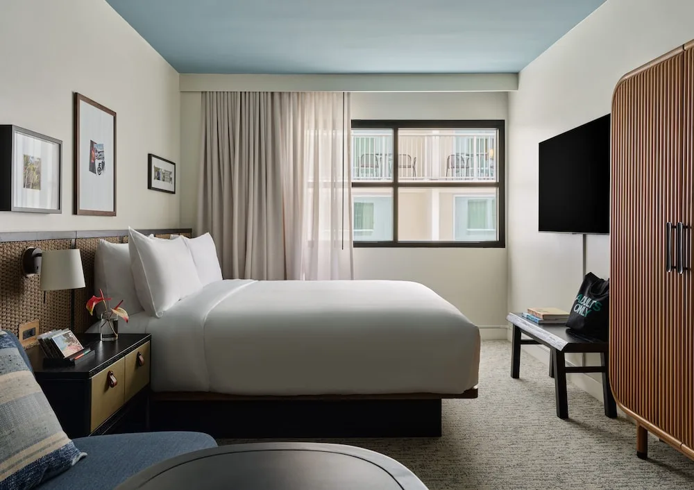Guest room with a king bed, sofa, wardrobe, TV, and window at Romer House Waikiki.