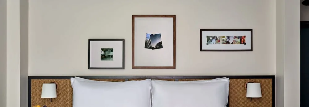 Guest room bed with woven headboard panels and framed wall art at Romer House Waikiki.