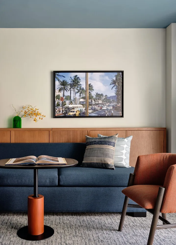 Guest room lounge area with blue sofa, rust chair, and framed Waikiki artwork at Romer House Waikiki.