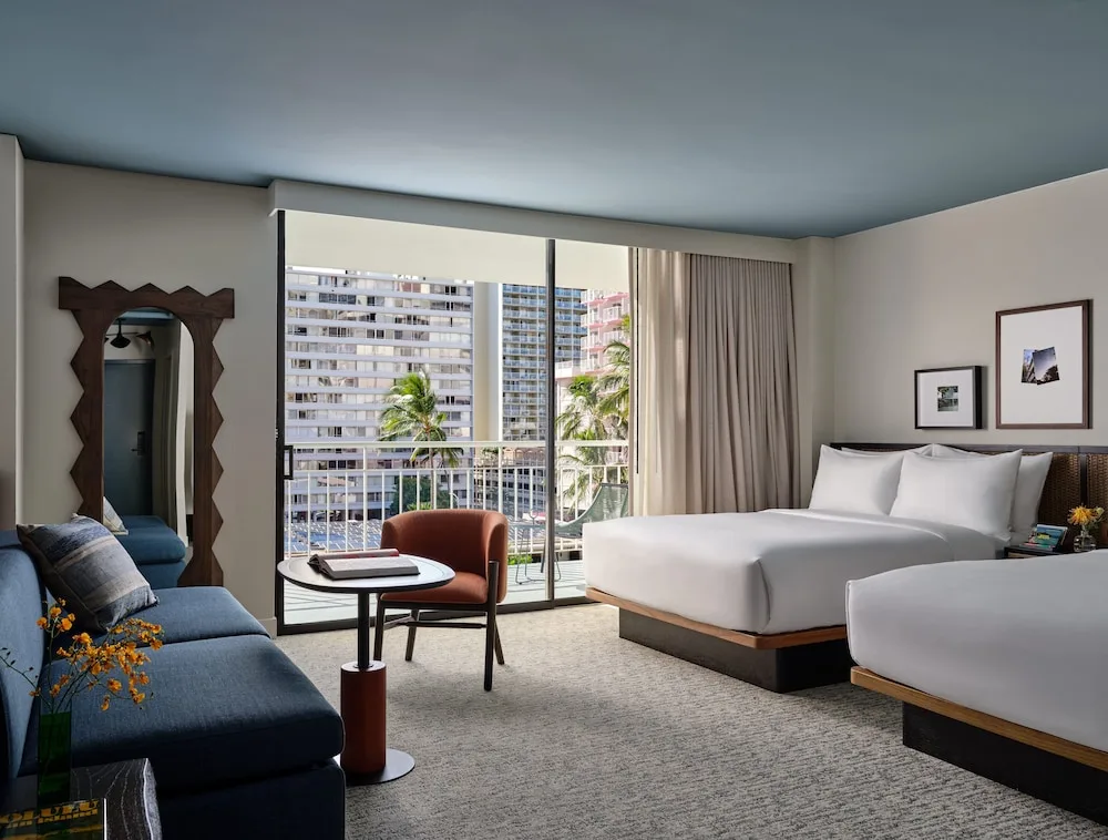 Two beds, sofa, and balcony view in a guest room at Romer House Waikiki.