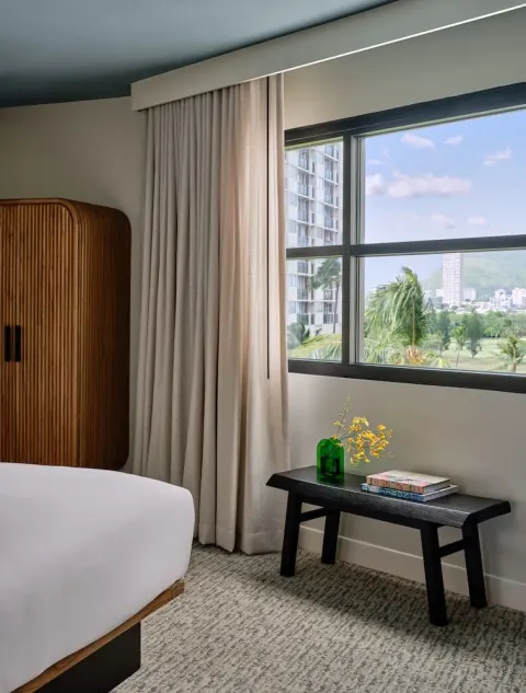 Guest room window, partial bed, wardrobe, and bench at Romer House Waikiki.