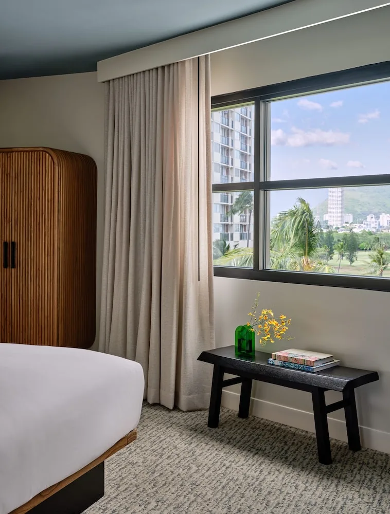 Guest room window, partial bed, wardrobe, and bench at Romer House Waikiki.