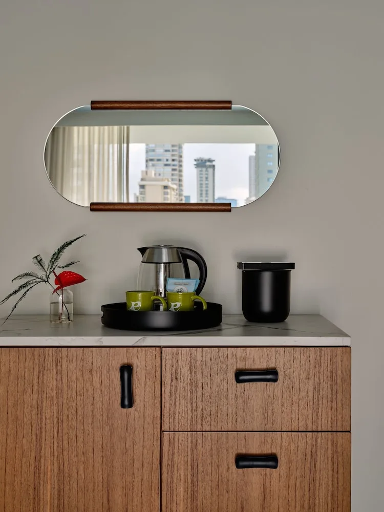 In-room beverage station with kettle, mugs, mirror, and wood cabinet at Romer House Waikiki.