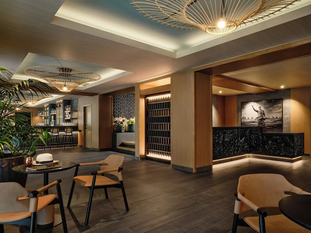 Lobby seating area with reception desk, bar, plants, and woven pendant lights at Romer House Waikiki.