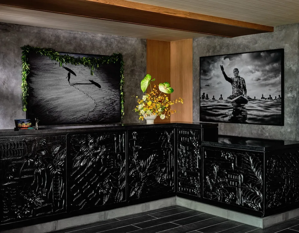 Reception desk with carved black panels and surf photography at Romer House Waikiki.