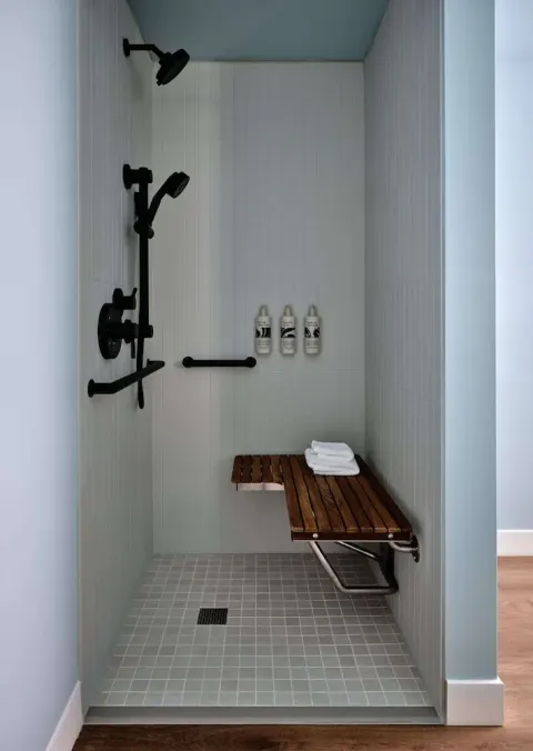 Walk-in shower with black fixtures and a wooden bench at Romer House Waikiki.