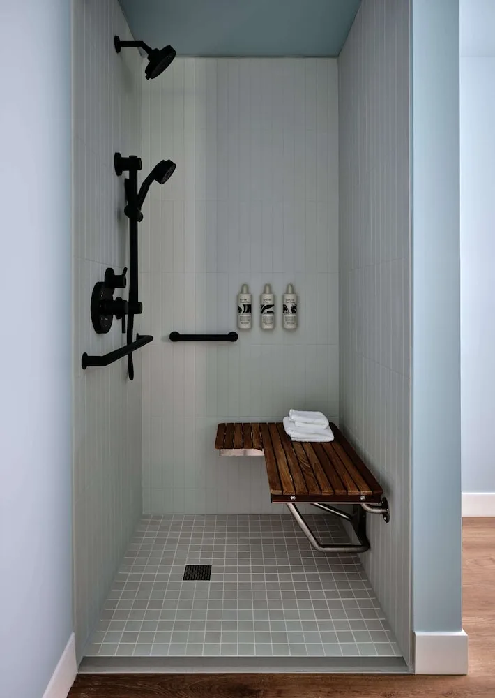 Walk-in shower with black fixtures and a wooden bench at Romer House Waikiki.