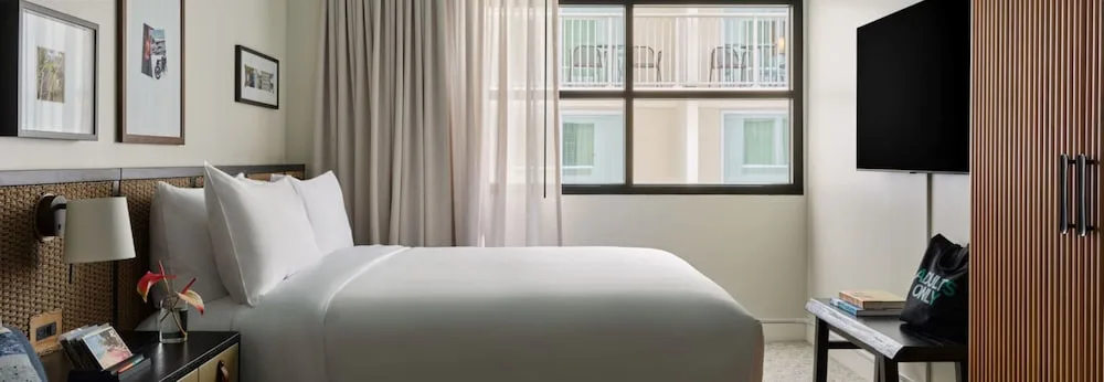 Wide guest room view with king bed, wardrobe, TV, and window at Romer House Waikiki.