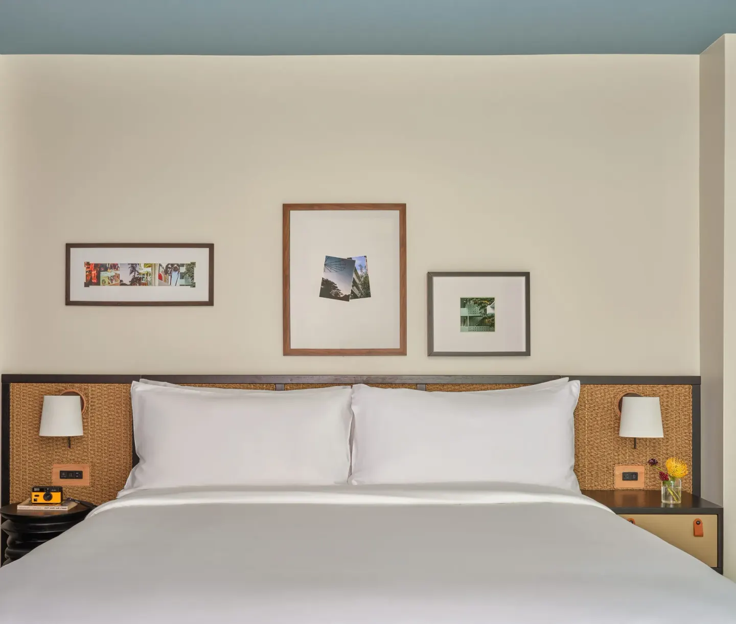 King bed with woven headboard and framed art in a Deluxe Room Balcony at Romer House Waikiki.