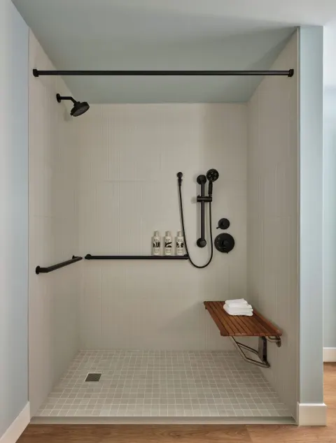 Roll-in shower with grab bars and bench in a Deluxe Room at Romer House Waikiki.
