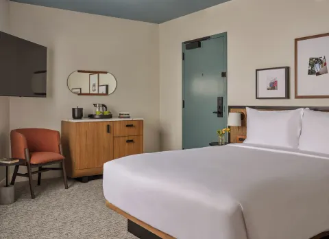 Deluxe Room king bed with dresser, chair, TV, and entry door at Romer House Waikiki.
