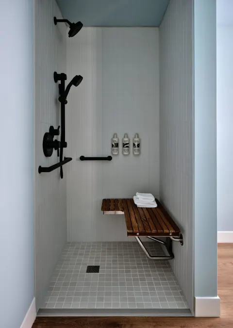 Transfer shower with bench, grab bars, and black fixtures at Romer House Waikiki.