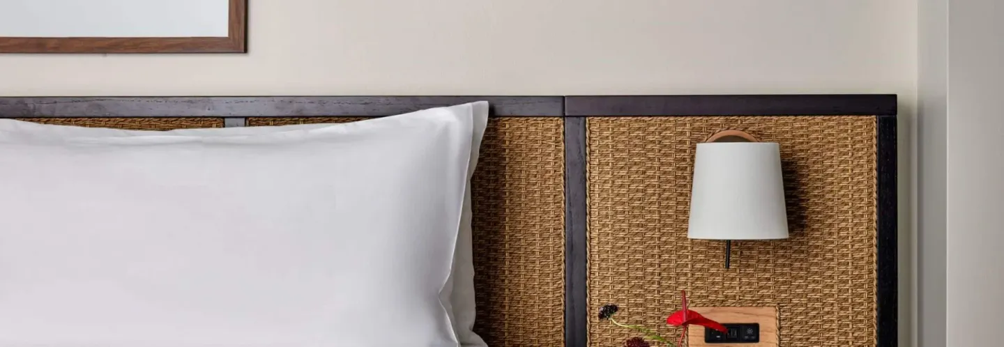 Close-up of a Deluxe Room bed headboard and wall lamp at Romer House Waikiki.