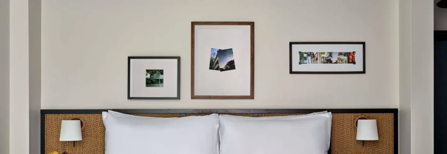 Deluxe Room bed with woven headboard and framed wall art at Romer House Waikiki.