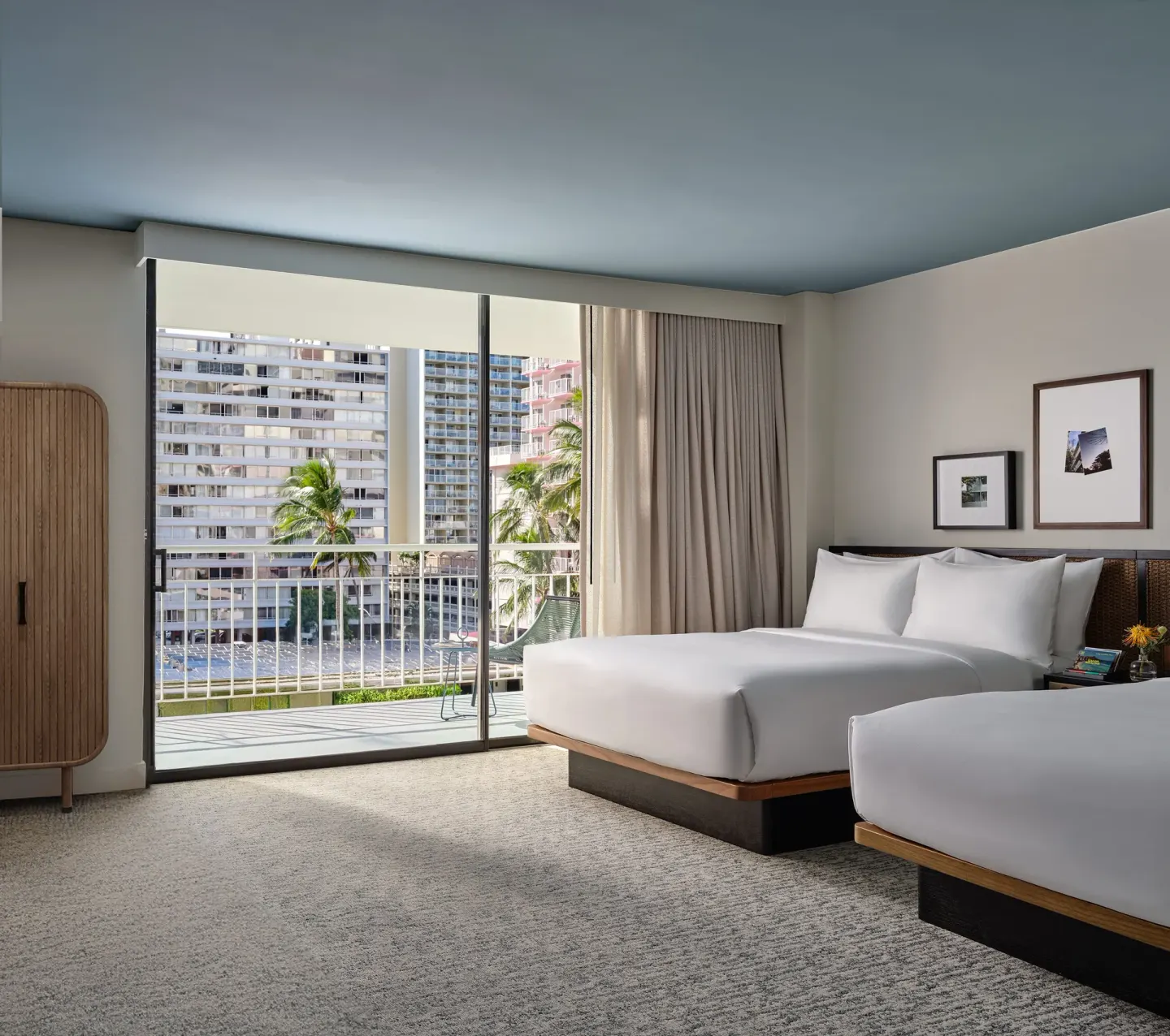 Deluxe Room with two double beds, balcony doors, and city buildings at Romer House Waikiki.