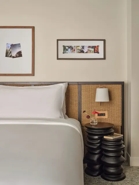 Bedside table, lamp, flowers, and woven headboard in a Two Bedrooms Suite at Romer House Waikiki.