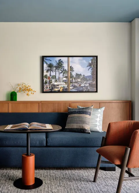 Blue sofa, orange chair, round table, and framed photo in a Two Bedrooms Suite at Romer House Waikiki.