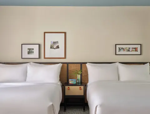 Two white beds with a shared nightstand and framed art in a Two Bedrooms Suite at Romer House Waikiki.