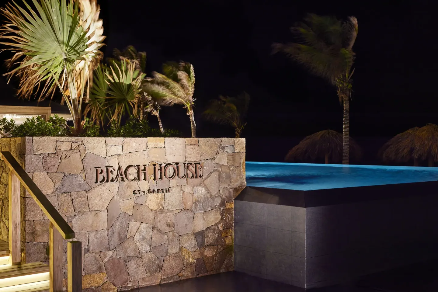 Illuminated stone Beach House sign beside a pool at night at Rosewood Le Guanahani St Barth.