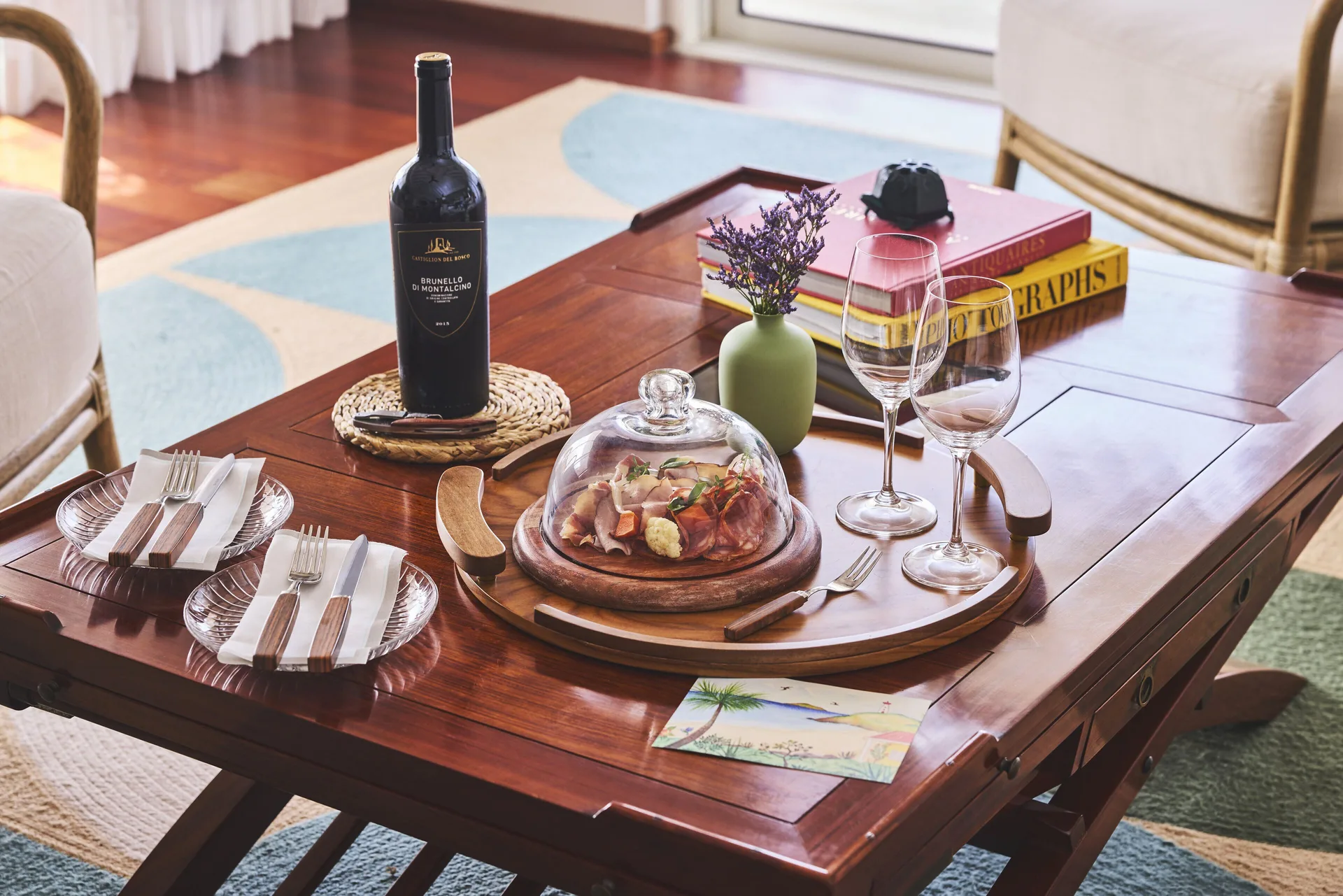 Coffee table set with wine, plates, glasses, flowers, and covered food at Rosewood Le Guanahani St Barth.