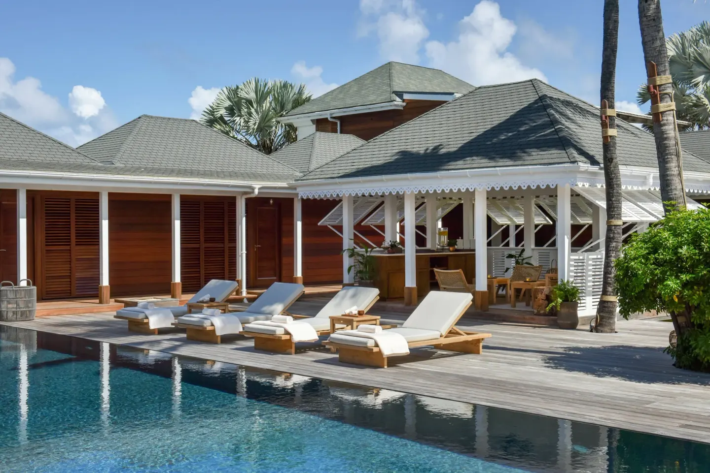 Poolside loungers beside wood buildings at Rosewood Le Guanahani St Barth.