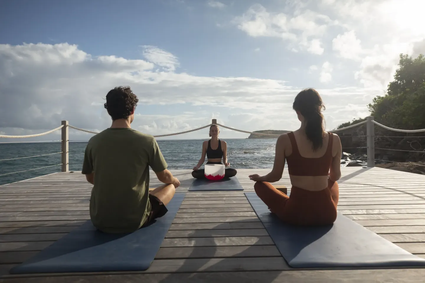 Guests sit on yoga mats facing an instructor by the sea at Rosewood Le Guanahani St Barth.
