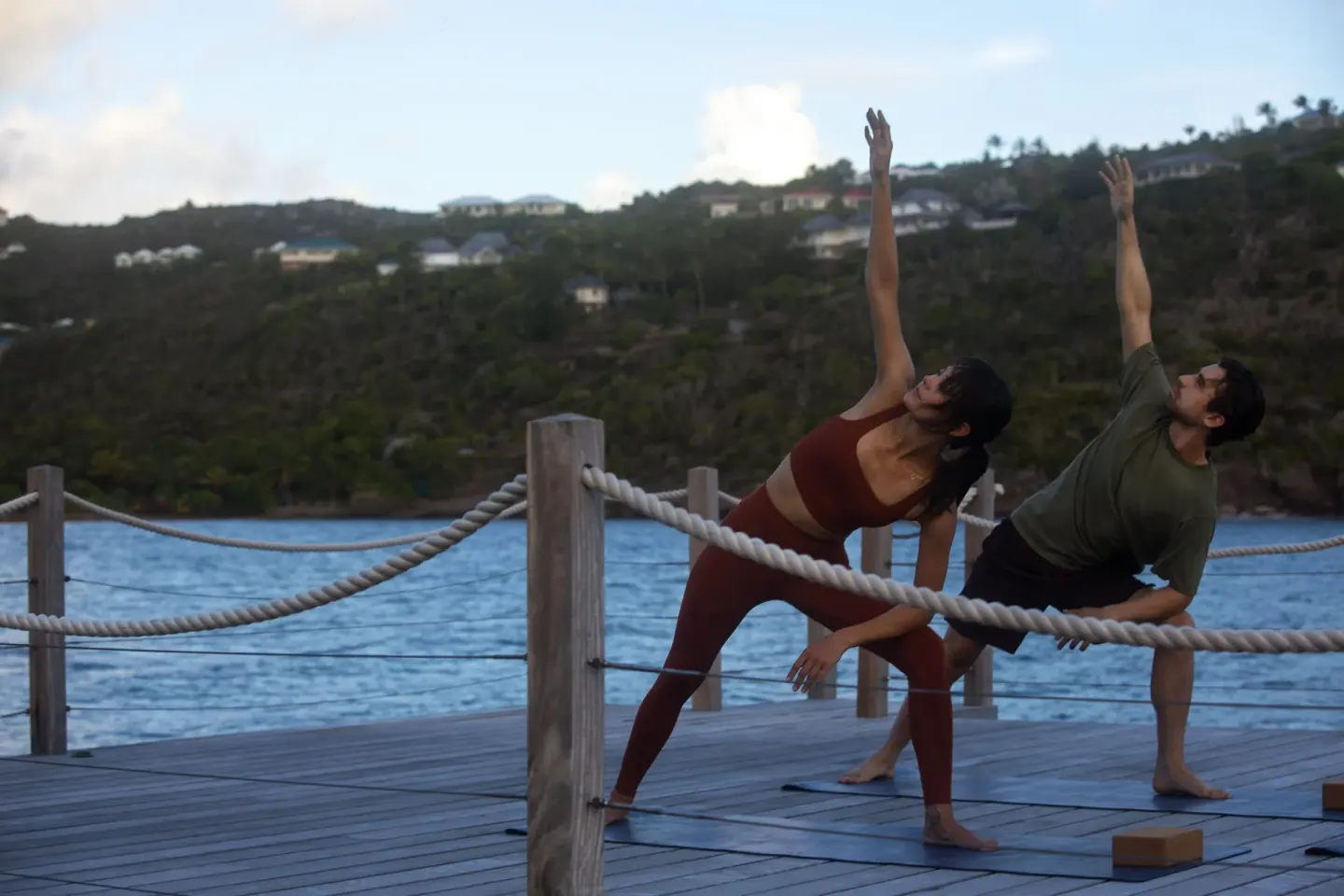 Two guests hold a yoga pose on a deck by the sea at Rosewood Le Guanahani St Barth.
