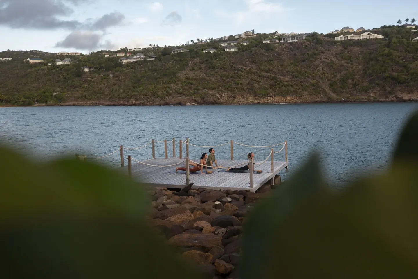 Guests practice yoga on a waterfront deck at Rosewood Le Guanahani St Barth.