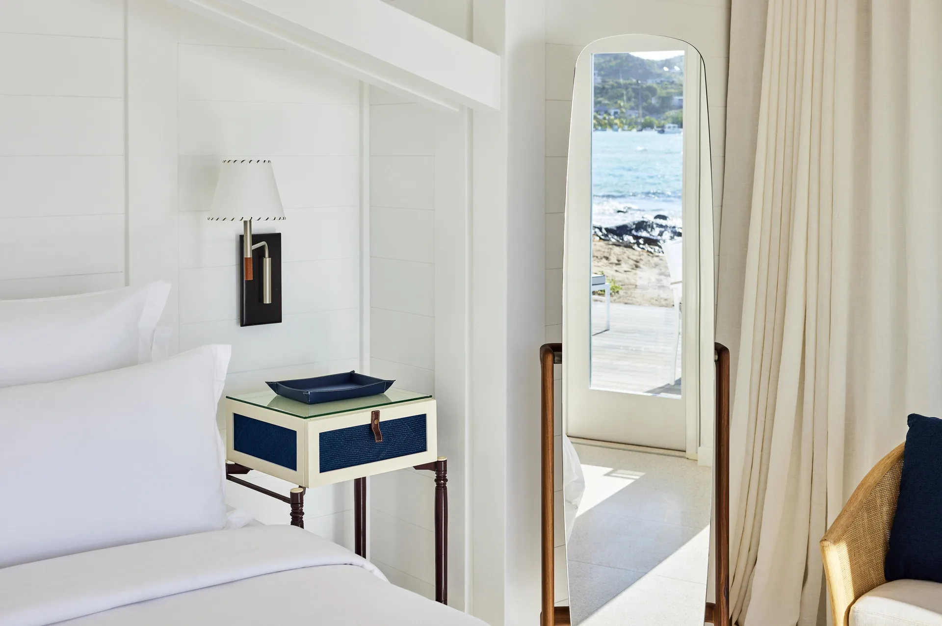 Lagoon Suite bedside table and floor mirror by cream curtains at Rosewood Le Guanahani St Barth.