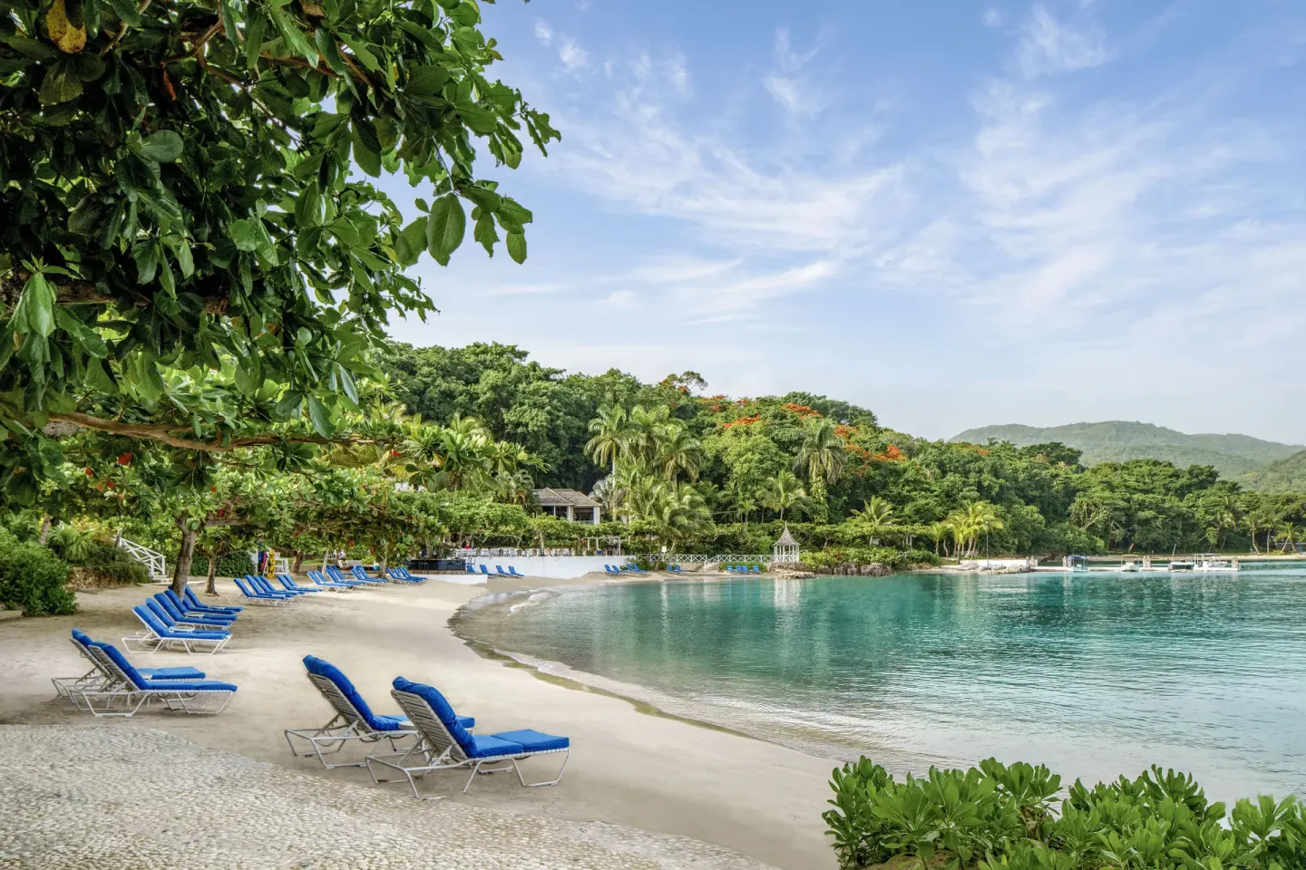 Blue lounge chairs line a sandy beach at Round Hill Hotel And Villas.