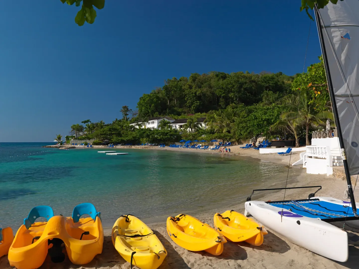 Beach with kayaks, a sailboat, and turquoise water at Round Hill Hotel And Villas.