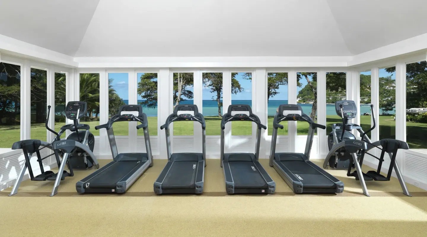 Fitness room with treadmills, ellipticals, and ocean-facing windows at Round Hill Hotel And Villas.