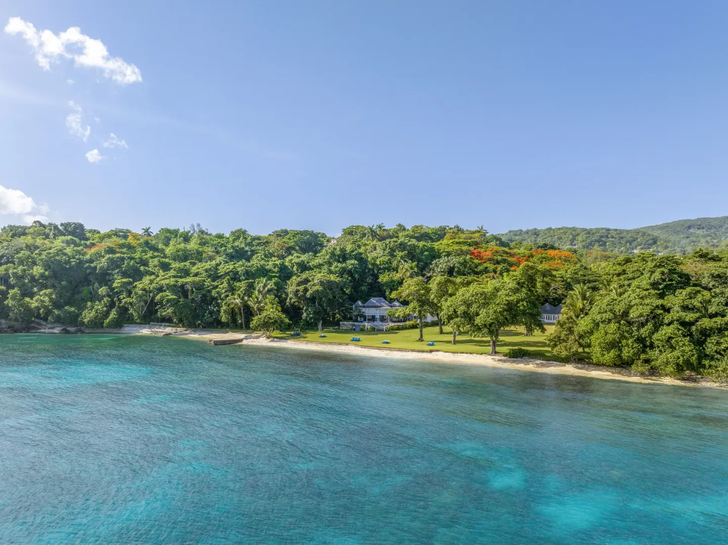 Clear blue water borders a quiet beach and green lawn at Round Hill Hotel And Villas.