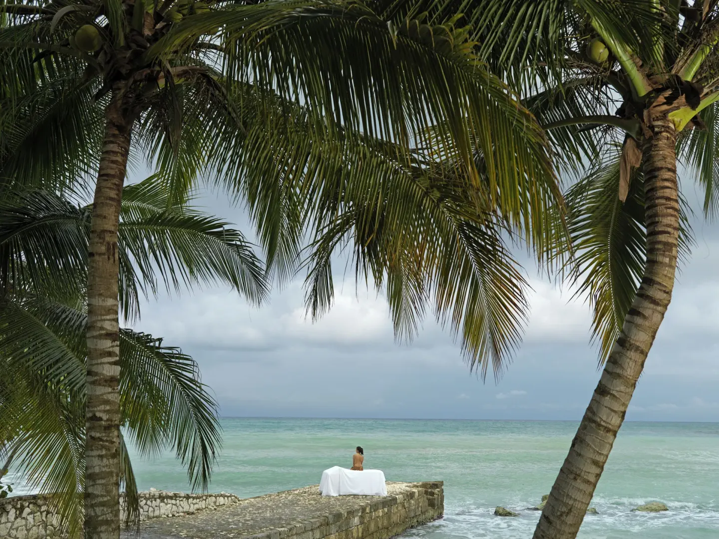 Stone seaside terrace with a massage table under palms at Round Hill Hotel And Villas.
