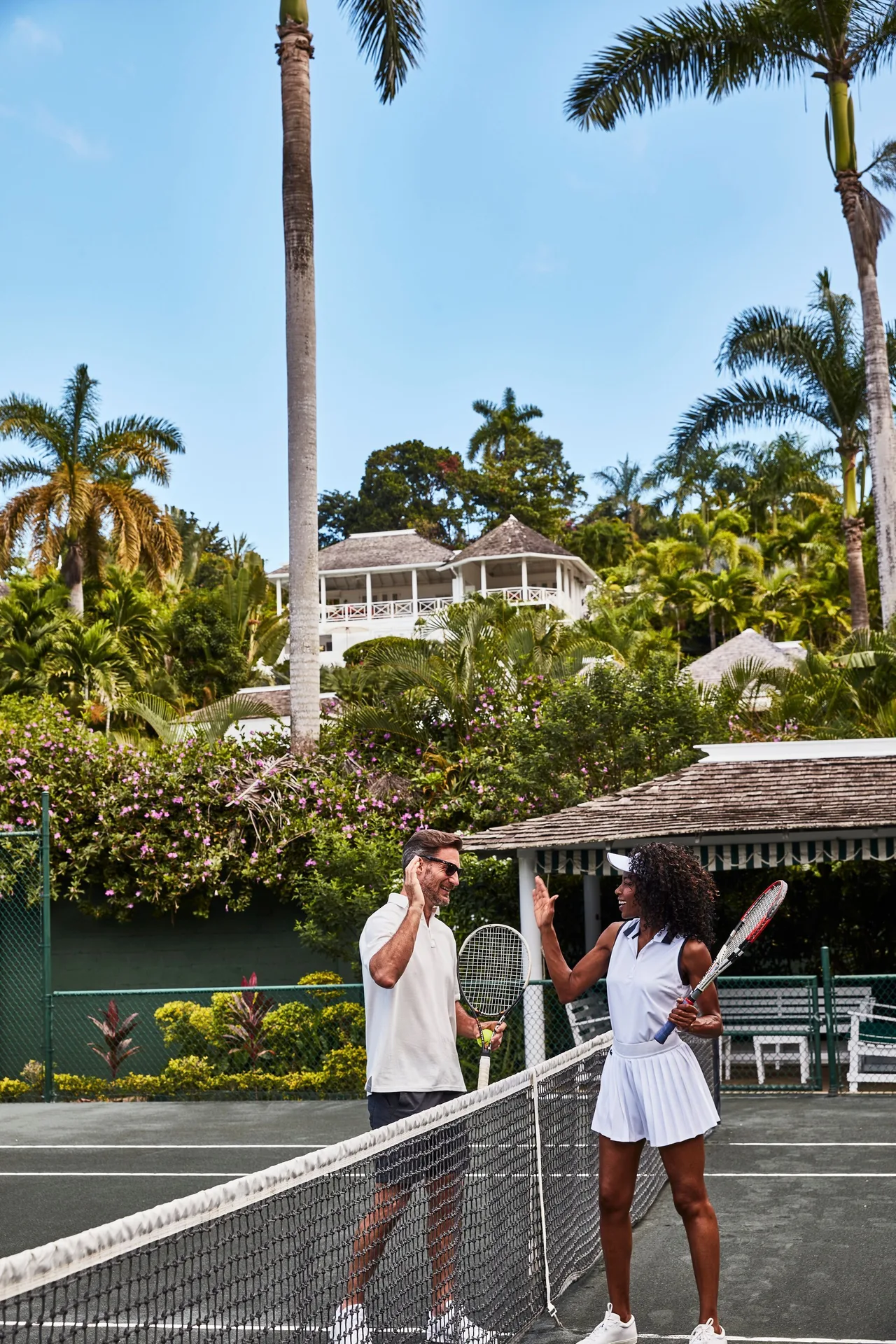 Two guests holding tennis rackets on a court at Round Hill Hotel And Villas.