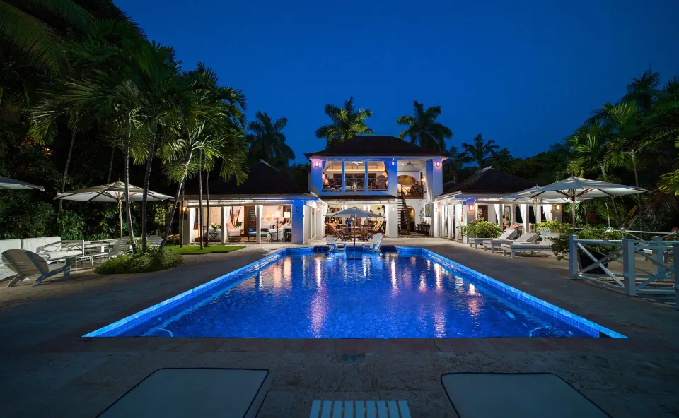 Evening view of the Signature Villa private pool at Round Hill Hotel And Villas framed by palms and lit rooms.