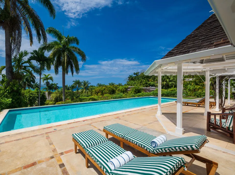 Signature Villa private pool at Round Hill Hotel And Villas with striped loungers, palms, and ocean beyond.