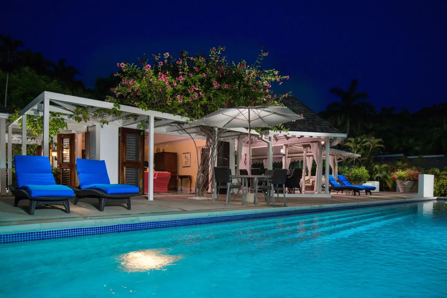 Night view of a Signature Villa pool terrace at Round Hill Hotel And Villas with blue loungers and umbrellas.